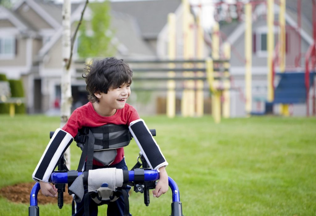 Disabled boy in walker in front of playground cerebral palsy patient