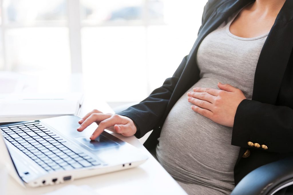 Pregnant woman working on laptop. Cropped image of pregnant businesswoman typing something on laptop while sitting at her working place in office birth defects